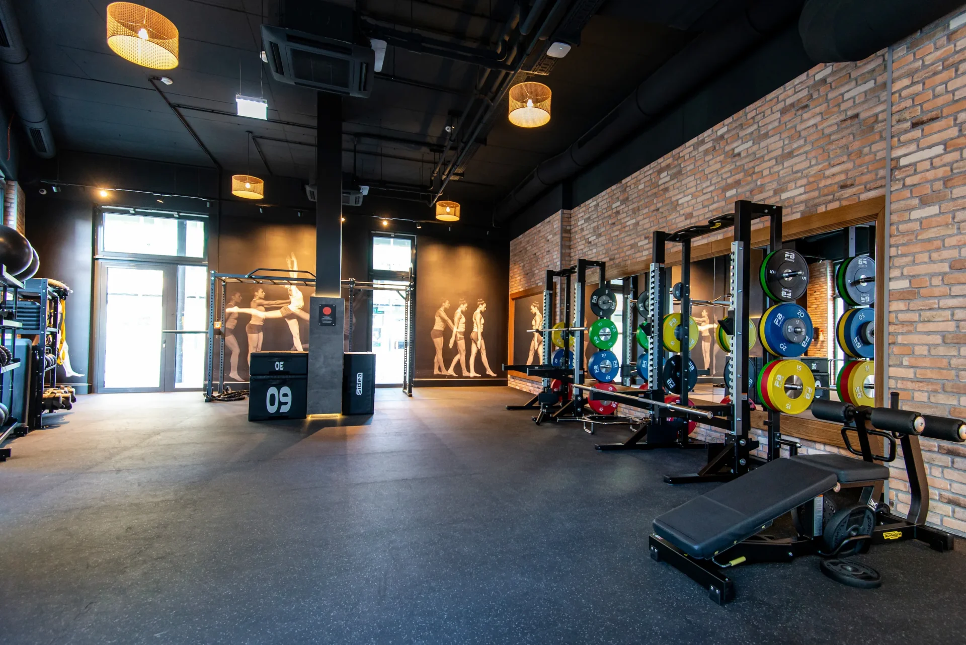 Gym area with weightlifting racks, colourful bumper plates, and brick wall under modern lighting at EVO Modecenterstraße