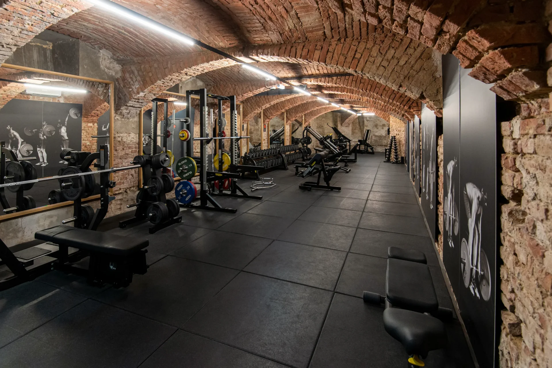 Performance zone with benches and squat racks under arched brick ceiling at EVO Fitness Schleifmühlgasse