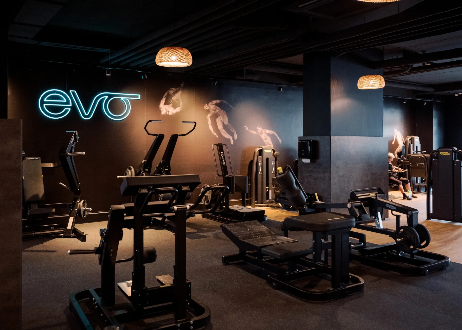 Strength training machines at EVO gym with neon EVO logo on wall at EVO Fitness