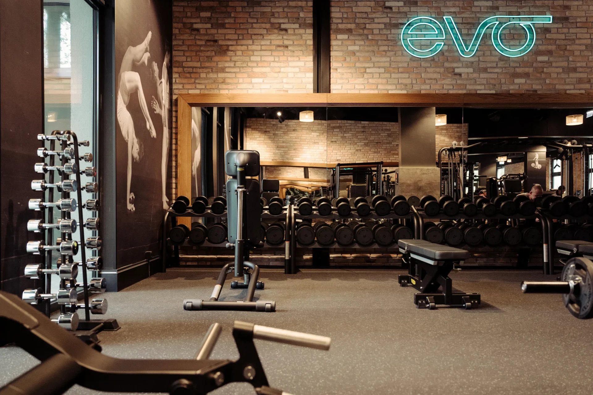 Wall of mirrors with dumbbells and EVO neon sign above at EVO Fitness