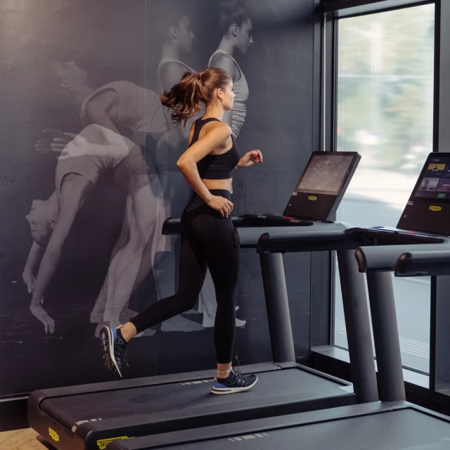 Woman running on a treadmill near a large window at EVO Fitness