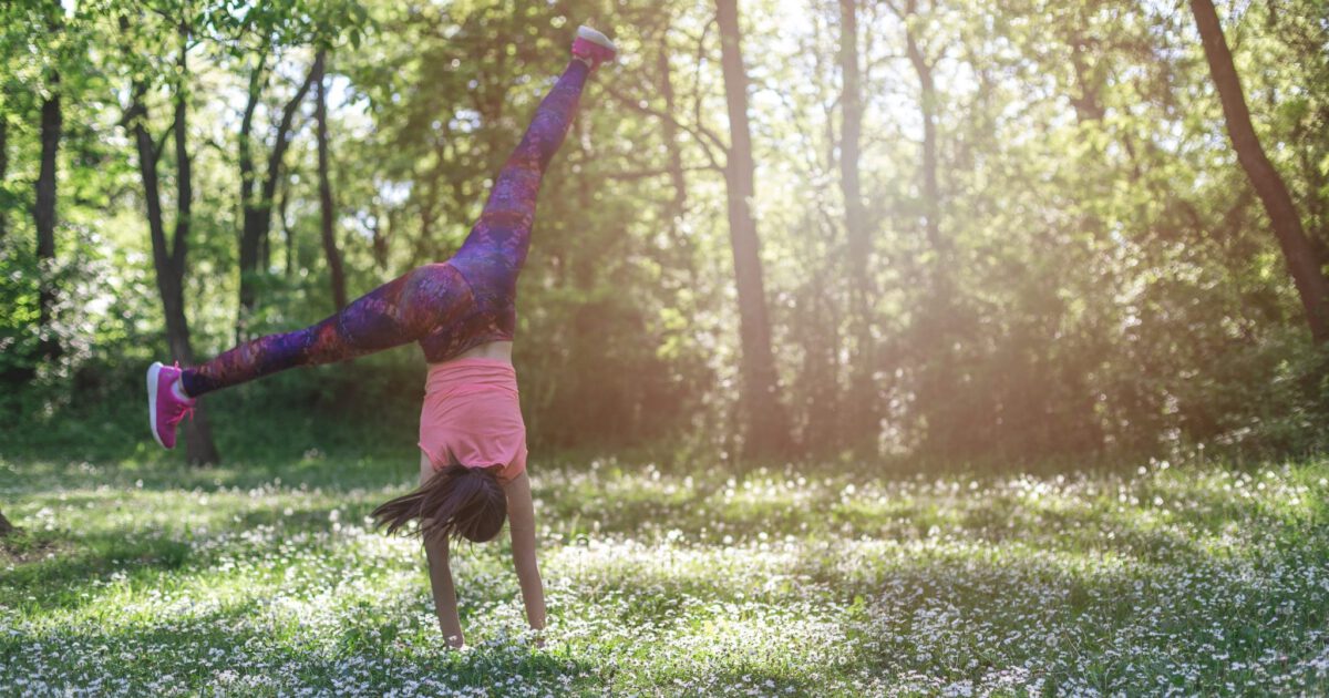 sport girl makes a cartwheeling on a field of flowers - sunny day in a park/forest