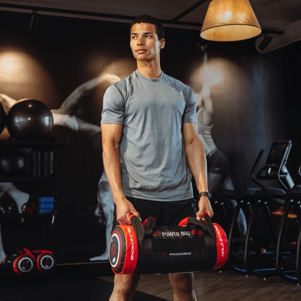 Man lifting a 10kg power bag in the functional training area of EVO Fitness, cardio machines and athlete wall art behind him