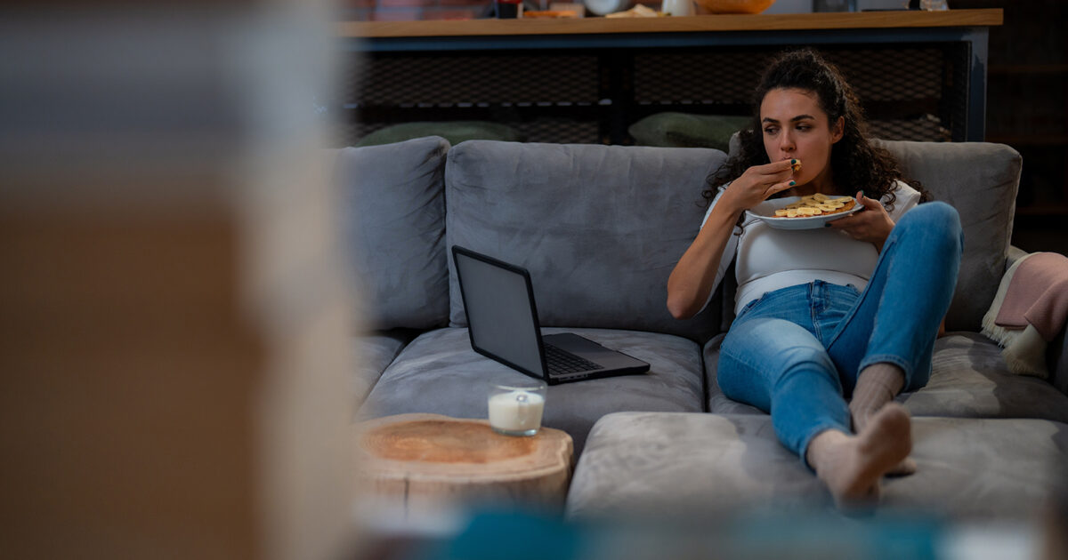 eating while watching TV - girl sitting on the couch eating and watching TV