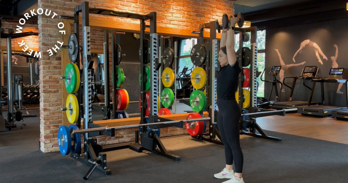 100 Reps Dumbbell-Kraft-Workout - Frau hebt Kurzhanteln bei EVO Fitness umgeben von bunten Plates und Backsteinwaenden