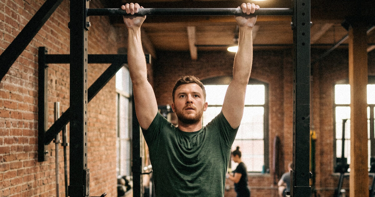 4 Vorteile von Griffkraft (und warum sie wichtig ist) - Mann macht Klimmzüge an einer Stange in einem Industrial-Style Gym mit Backsteinwänden