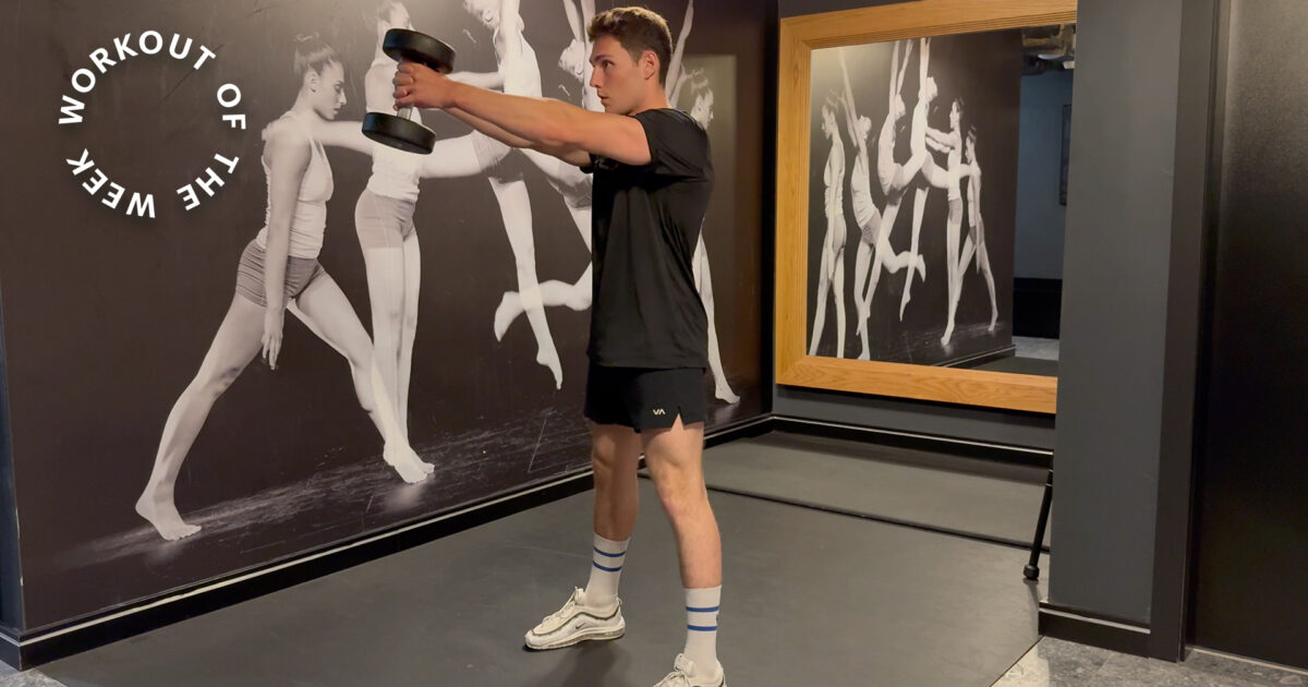 Workout of the week: 15-min dumbbell metabolic strength workout - Man doing front raise with dumbbell in gym in front of mirror and workout mural