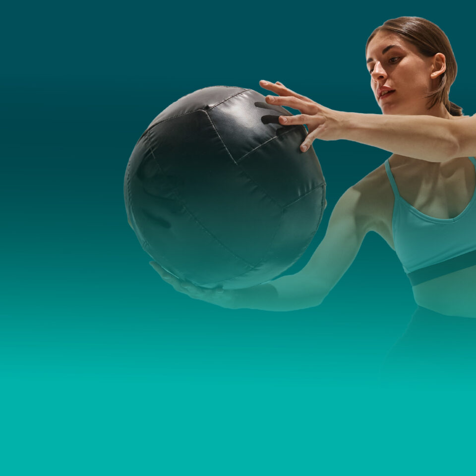 Weibliche Athletin hält Medizinball während funktionellem Workout vor türkisfarbenem Hintergrund